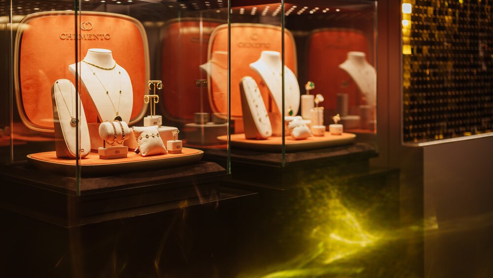 Elegante Schmuckstücke werden auf Ständern in Glasvitrinen mit orangefarbenem Hintergrund und warmer Beleuchtung präsentiert.