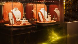 Elegante Schmuckstücke werden auf Ständern in Glasvitrinen mit orangefarbenem Hintergrund und warmer Beleuchtung präsentiert.