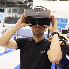 Ein Mann mit kurzem Bart in einem schwarzen Hemd verwendet an einem Messestand eine VR Brille.