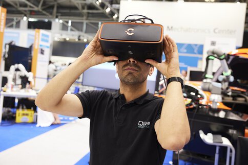 A man with a short beard in a black shirt uses VR glasses at a trade fair stand.