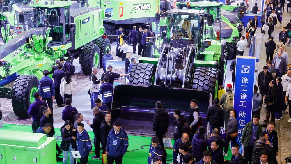 A crowd at an industrial trade show featuring large green construction machines.