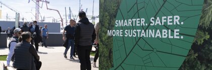 Menschen im Außenbereich einer Messe neben Plakat mit Nachhaltigkeitsbotschaft.