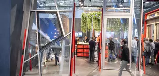 Konstruktionen für Glasfenster und -türen stehen zu Präsentationszwecken an einem Stand auf der BAU. Davor und dahinter sind einige Besucher zu sehen.