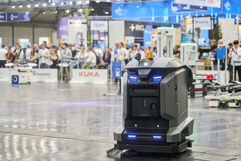  Autonomous mobile robot drives through an exhibition hall, with visitors and exhibitor stands in the background.