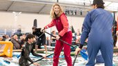 Eine lachende Frau steht mit einem Paddel in der Hand auf einem Board im Pool in einer Halle der f.re.e während hinter ihr weitere Personen im Wasser sind.