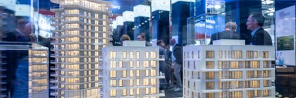 View of an architectural model in a glass display case with three illuminated skyscrapers. Numerous visitors can be seen behind it.