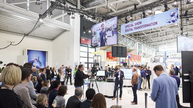 View from the audience onto a stage where a man is being filmed explaining something