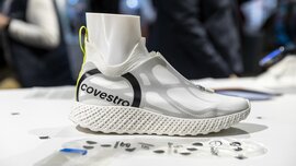 Nahaufnahme eines weißen und grauen Sportschuhs mit der Aufschrift „covestro“ mit einem Puppenfuß darin auf einer Präsentationsfläche der LOPEC.