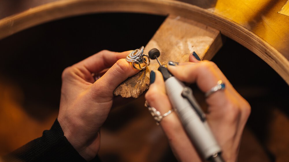 Close-up of two hands finishing a curved ring on a wooden table.