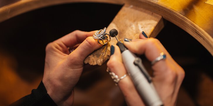  Two hands hold an artistically curved silver ring and carefully sand it down with a sander.
