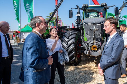 Mehrere Personen im Gespräch vor einem großen Traktor auf dem Freigelände einer Land- und Forsttechnikmesse.