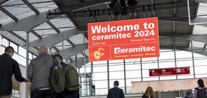 Menschen gehen durch die Eingangshalle der Messe München unter einem großen 