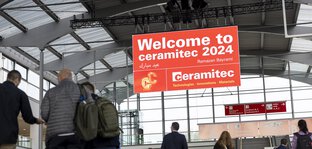 Menschen gehen durch die Eingangshalle der Messe München unter einem großen 