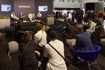 Seated and standing people at a panel discussion at a conference with presentations in the background.