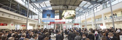 Zahlreiche Menschen stehen und warten auf den Einlass zur productronica. Werbebanner hängen unter der Decke.