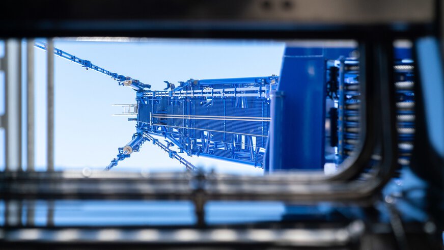 View through a rectangular frame of a tall blue industrial plant with towering cables.