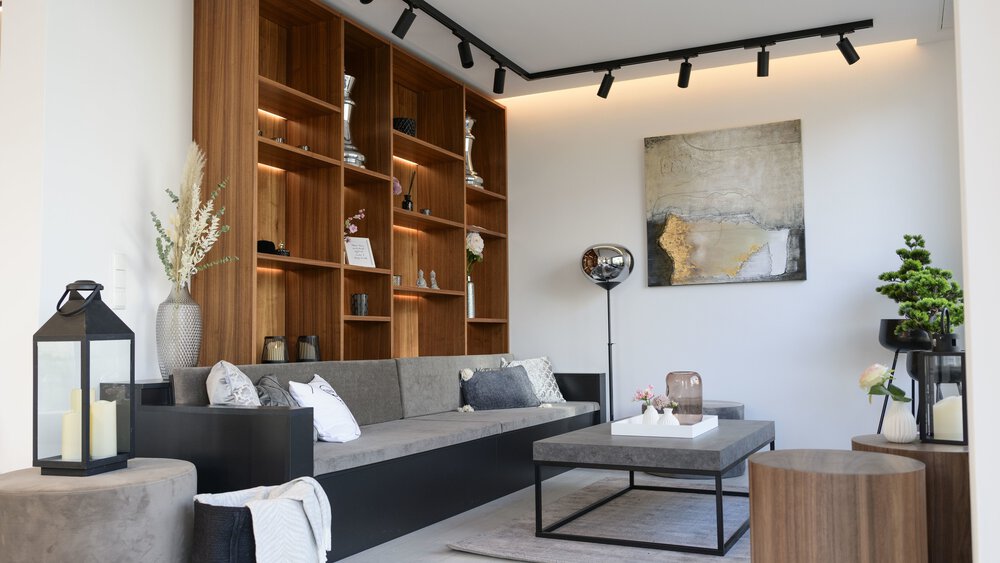 Modernes Wohnzimmer mit grauem Sofa, hölzernen Wandregalen, Couchtisch und Pflanzen. Neutrale Farben und natürliches Licht.