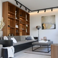 Modernes Wohnzimmer mit grauem Sofa, hölzernen Wandregalen, Couchtisch und Pflanzen. Neutrale Farben und natürliches Licht.