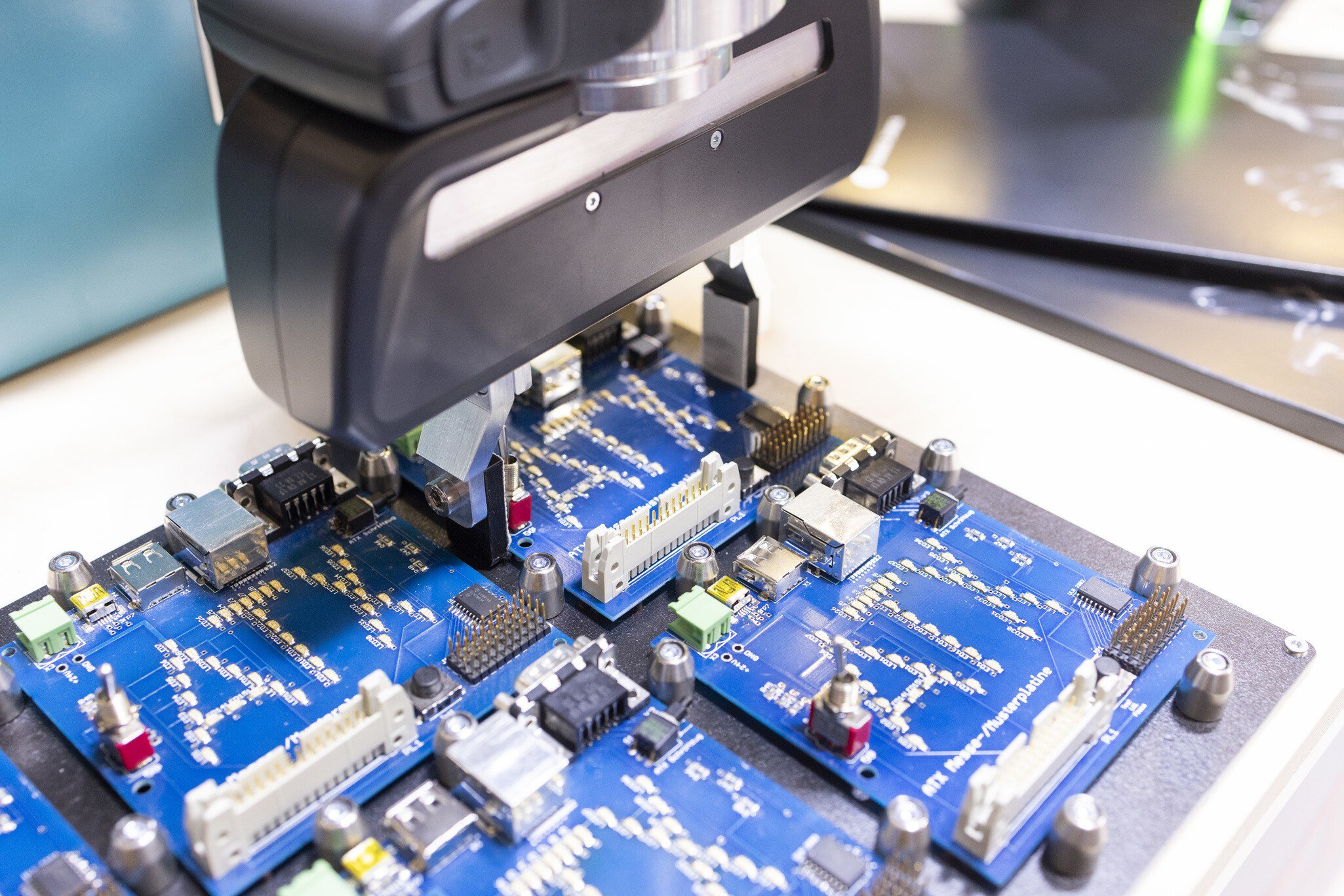Close-up of a gripping device that arranges several blue circuit boards with the imprint “ATX” symmetrically.