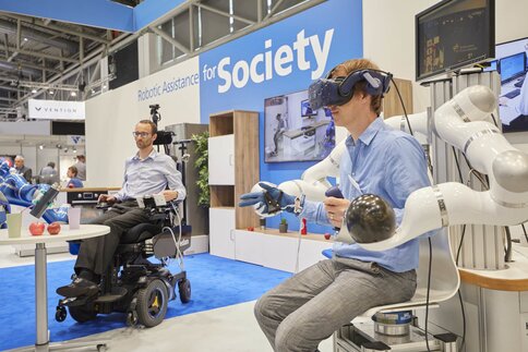 A person with a VR headset interacts with robotic arms and demonstrates robotics at a technology exhibition.