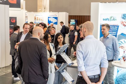 Menschen unterhalten sich an einem Messestand einer Firma, umgeben von Bannern und Informationstafeln.