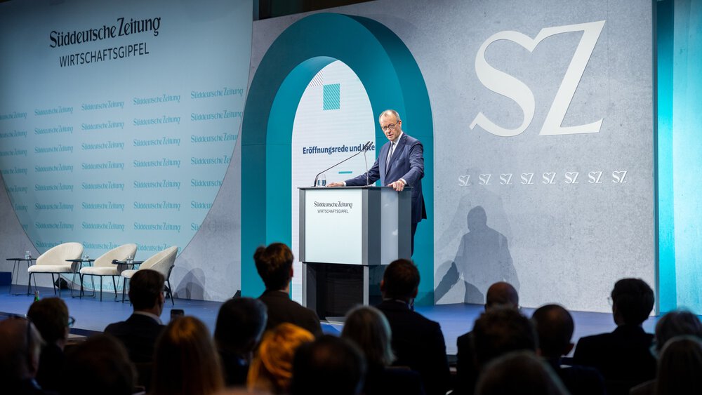 Bundeskanzler Friedrich Merz spricht am Rednerpult auf der Bühne des SZ Wirtschaftsgipfels vor Publikum; im Hintergrund sind das SZ-Logo und die Bühnenkulisse zu sehen. 