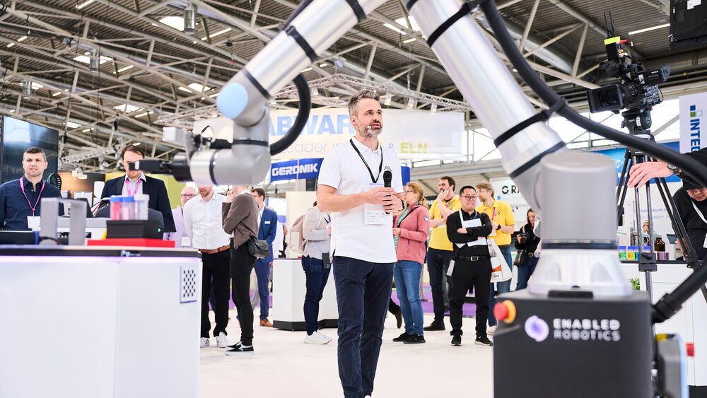 Vortrag auf einem Messestand mit Publikum im Hintergrund