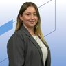 Junge Frau mit langen Haaren und Nadelstreifenblazer steht vor modernem, blauem Hintergrund mit geometrischen Formen und lächelt leicht in die Kamera.