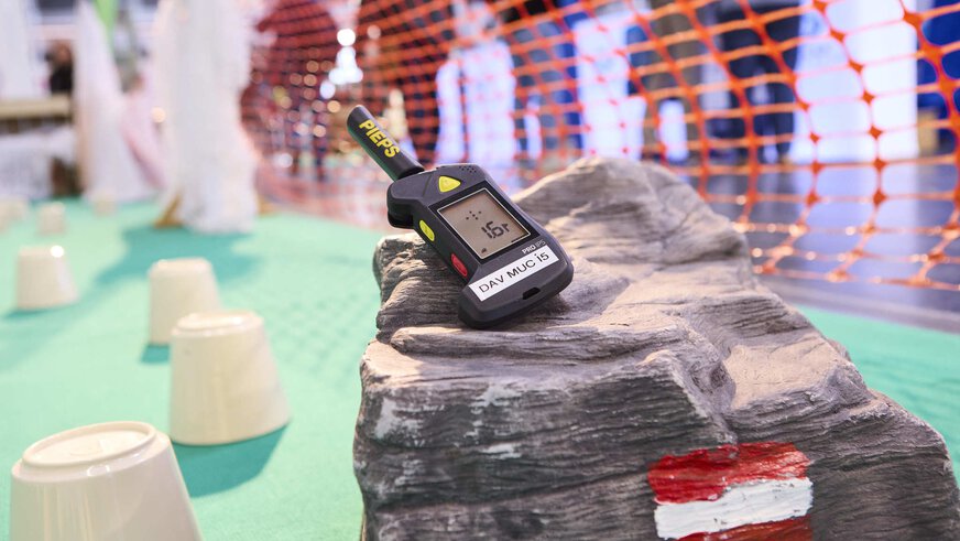 An avalanche transceiver lies on an artificial rock with a red-white-red hiking trail marking.