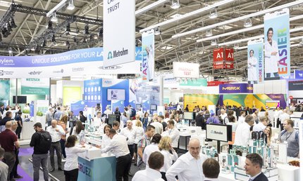 viele Personen in einer Messehalle informieren sich an verschiedenen Ständen