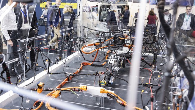 A Plexiglas model of a vehicle is on display at a trade fair stand, demonstrating the vehicle's complex cabling.