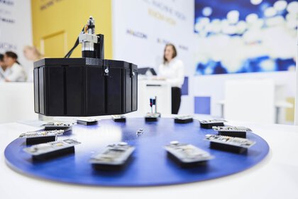 Kleine Elektronische Platinen auf einer Drehscheibe an einem Messestand. Im Hintergrund sind Messebesucher zu erkennen.