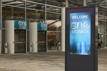 The picture shows a large convention hall with screens displaying the blue One Young World logo.