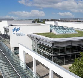 Moderne weiße Gebäude des Internationalen Kongresszentrums Messe München vor einem blauen Himmel mit Wolken.
