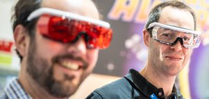 Two smiling people with colorful, modern-looking goggles in a technology exhibition.