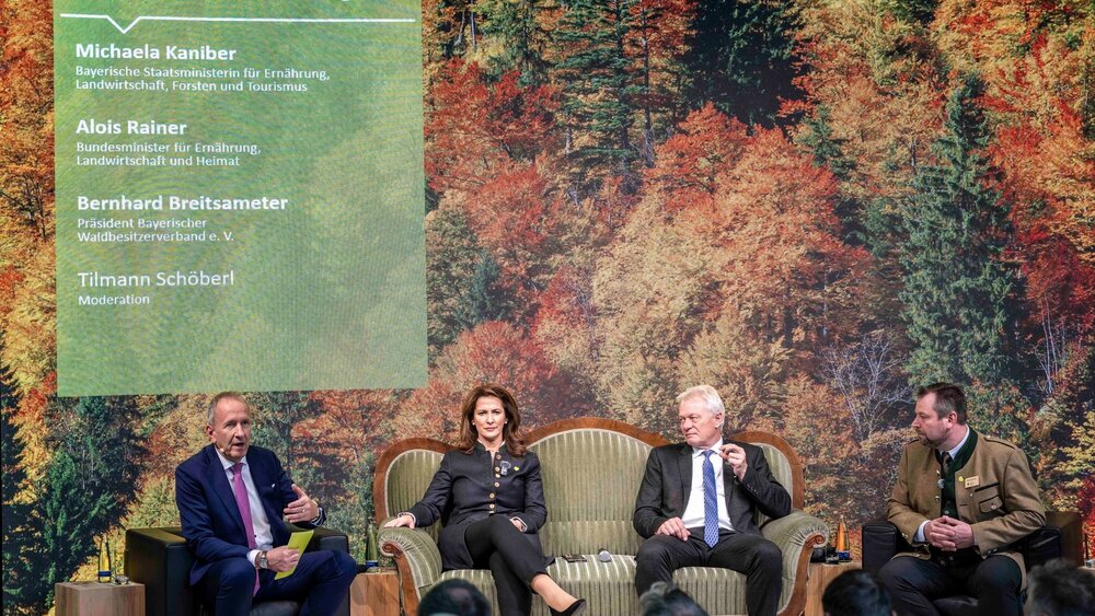 Four people seated during a panel discussion in front of a forest backdrop.
