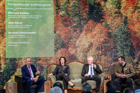Four people seated during a panel discussion in front of a forest backdrop.