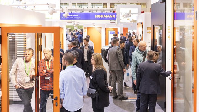 Several groups of trade fair visitors and exhibitors look at sample doors on stands at BAU.