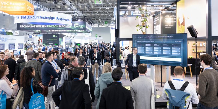 Messebesuchende stehen um einen Screen und lauschen einem Vortrag an einem Messestand.