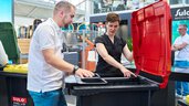 Zwei Personen begutachten am Sulo-Messestand einen modernen schwarzen Abfallbehälter mit rotem Deckel und integriertem Trennsystem.