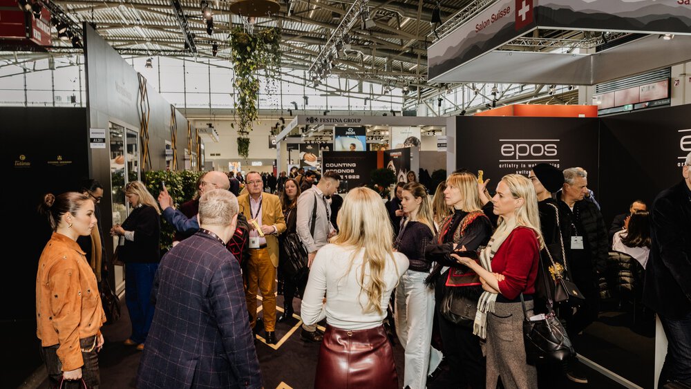 A crowd gathers in a busy exhibition hall with various stands and signs.
