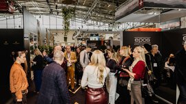 A crowd gathers in a busy exhibition hall with various stands and signs.
