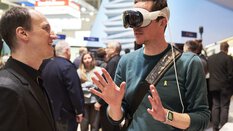 Während der BAU unterhalten sich zwei Männer, während einer von beiden eine weiße VR-Brille trägt und mit den Händen gestikuliert.