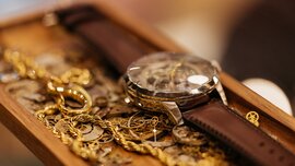 An ornate watch with a brown strap, along with other gold chains and gears, are all lying together in a wooden bowl.