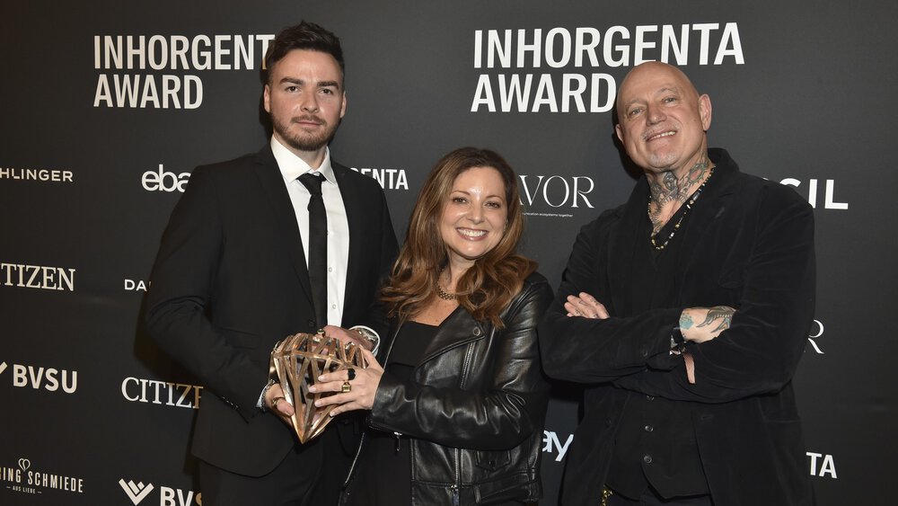 Three people holding the trophy for the “Fashion Jewelry of the Year” category smiling in front of a logo wall at the AWARD Gala.