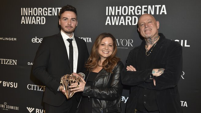 Three people holding the trophy for the “Fashion Jewelry of the Year” category smiling in front of a logo wall at the AWARD Gala.