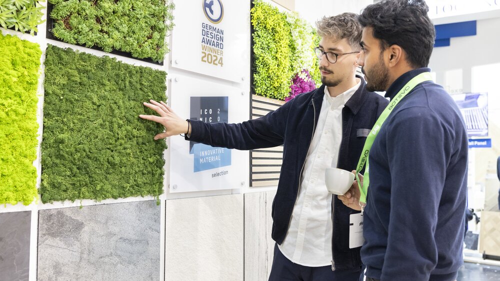 Two men look at a display wall with square material samples on the theme of “Innovative Material” for the “GERMAN DESIGN AWARD 2024”.