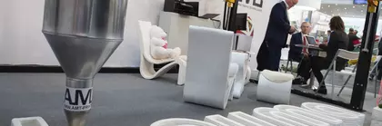 Ein 3D-Drucker erstellt das bauma Logo aus Beton, während zwei Personen im Hintergrund diskutieren.