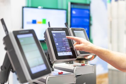 Close-up of a hand touching a digital industrial display showing weight and measurement data.