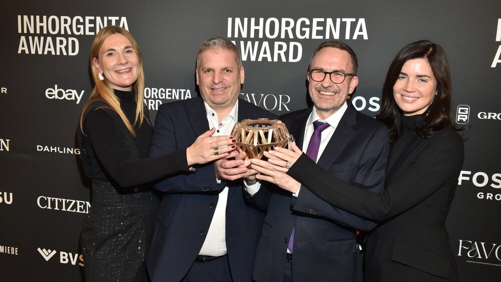 Four people smile and hold the trophy for the “Fine Jewelry of the Year” category in front of a logo wall at the INHORGENTA AWARD Gala.